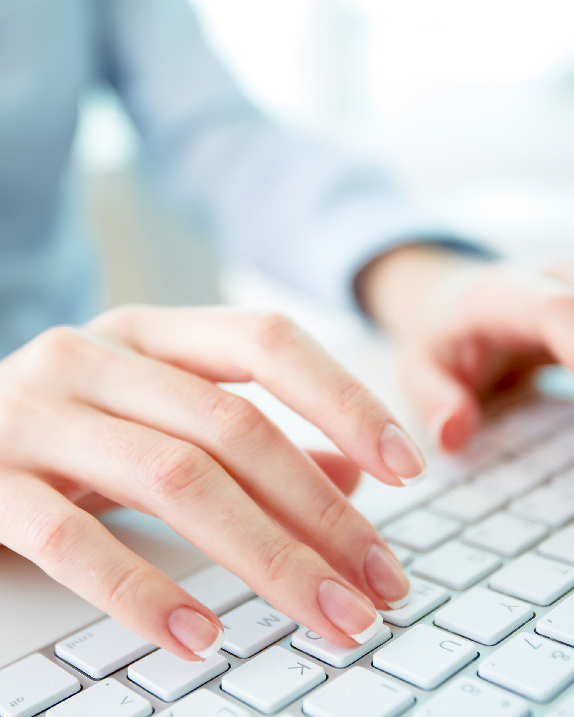 A woman's hands typing on a white keyboard in soft daylight.