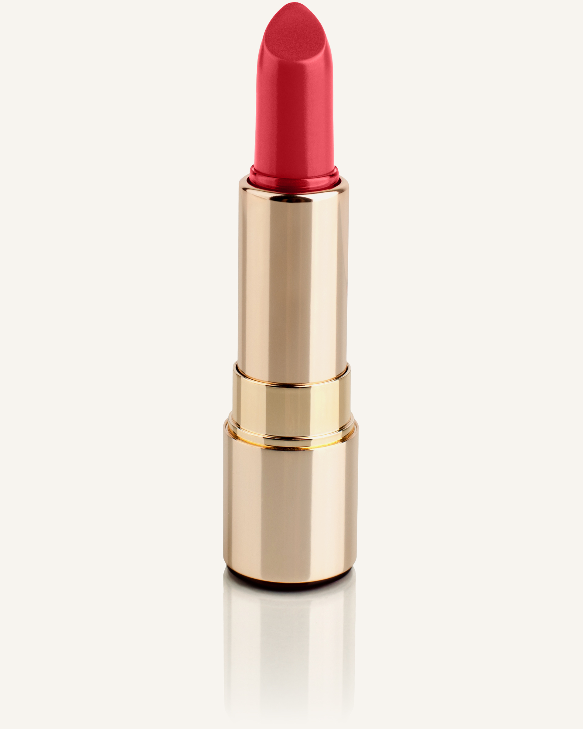 A single lipstick in a polished gold case, cap off and the bullet unworn, standing alone against a bone-colored ground.